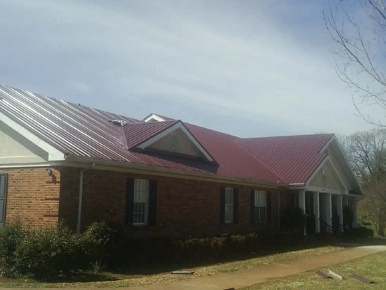 Red metal roof with gabled entries on a long brick building, from a Hail Damage Roof Repair job in Reydon