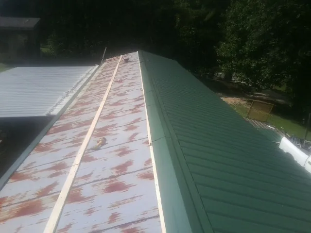 Old rusted panels beside newly installed green metal roofing — Wind Damage Roof Repair by Roofing Brothers in Reydon