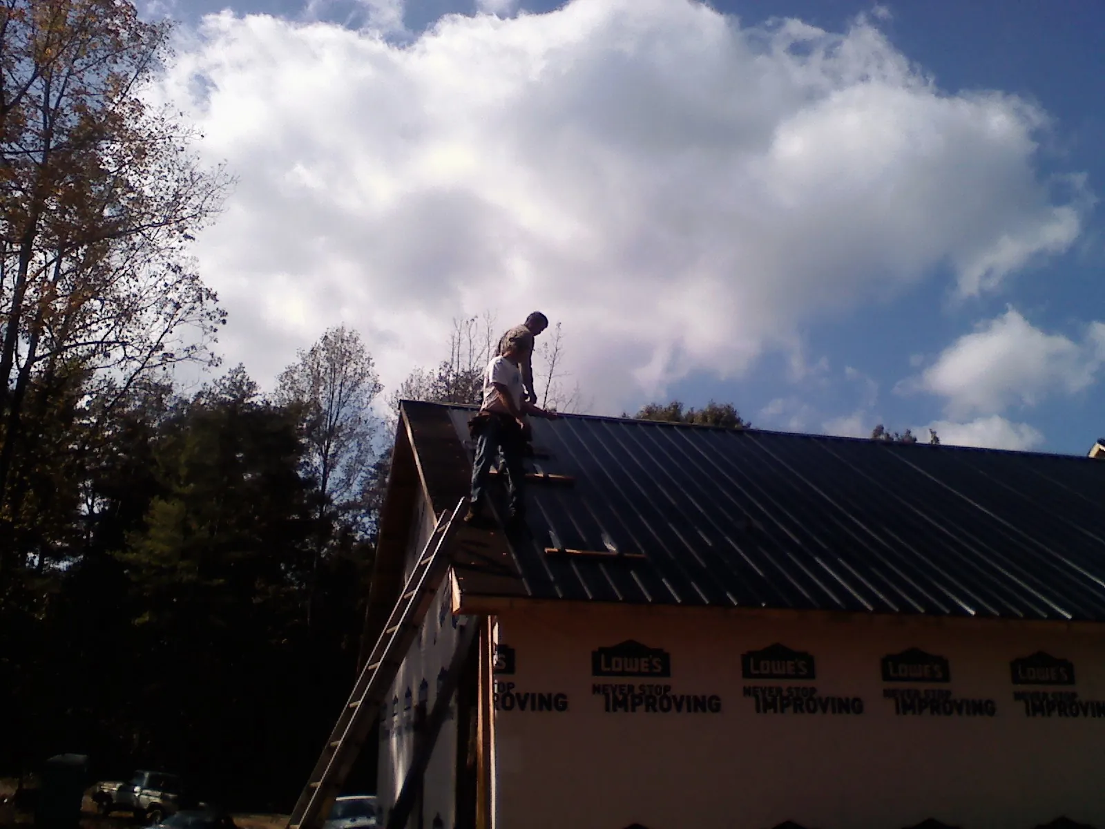 Roofer fastening dark metal panels high against a cloudy sky, from a Roof Inspection job in Reydon
