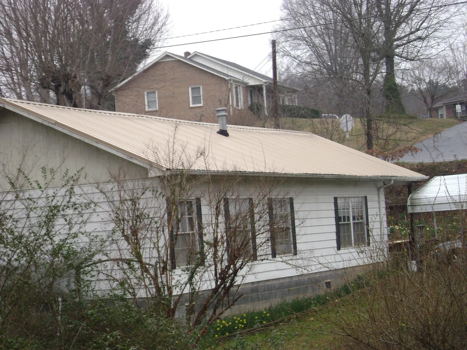 Tan metal roof on a white sided house set into a hillside — Commercial Roofing by Roofing Brothers in Reydon