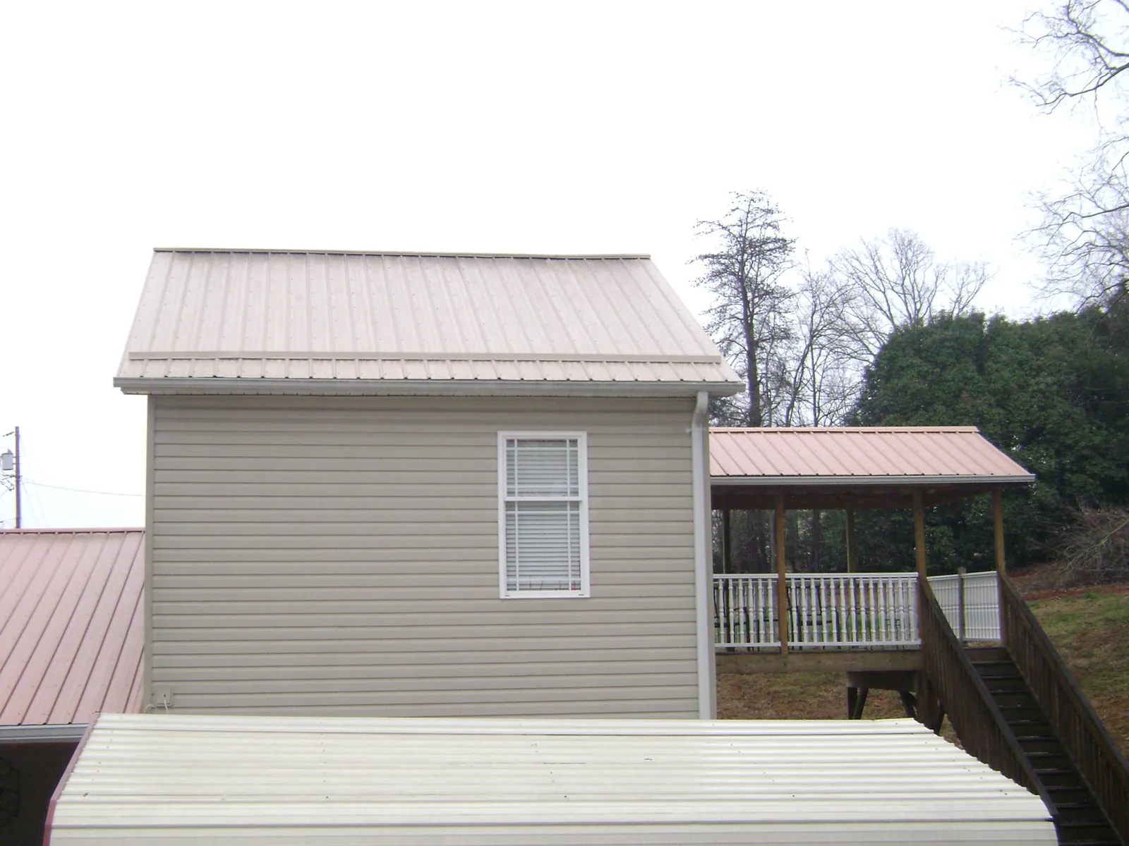 Tan metal roofs on a two story addition and attached porch, from a Roof Replacement job in Reydon
